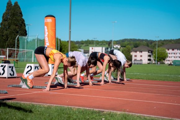 Auf dem Sportplatz auf der Rennbahn sind 4 Mädchen im sommerlichen Sportdress im Alter von ca. 13 Jahren bereit für den Startschuss für das Rennen am UBS Kids Cup.