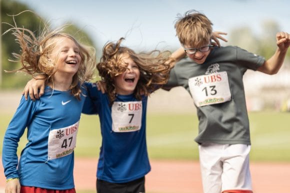 Photo de la UBS Kids Cup, 3 enfants heureux portant le dossard de départ UBS Kids Cup