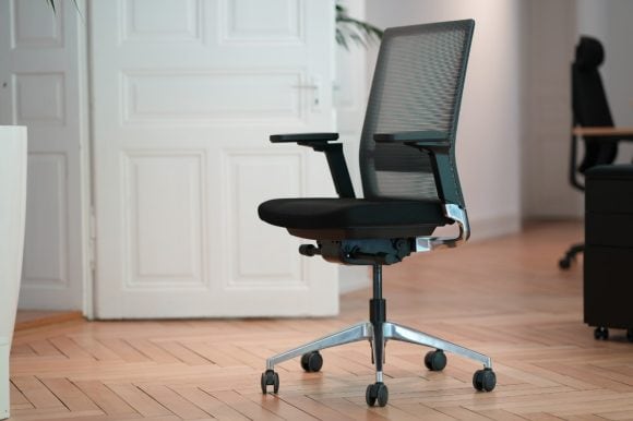 Ein moderner, dunkler Bürostuhl steht in einem Büro im Altbau-Stil.