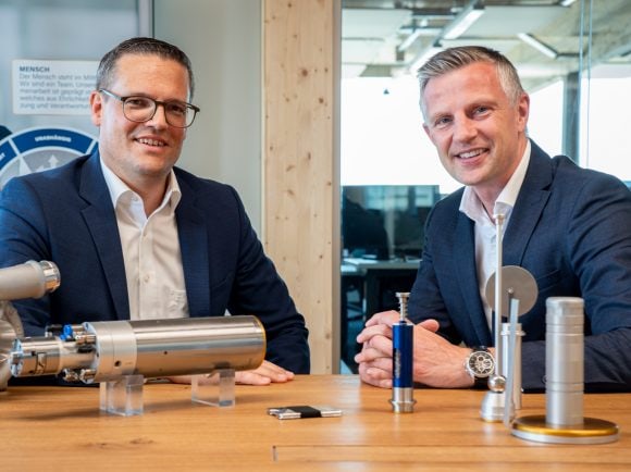 Zwei Männer sitzen an einem Tisch und unterhalten sich freundlich einander zugewandt.