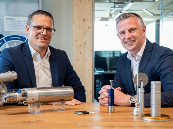 Deux hommes sont assis à une table et discutent amicalement, tournés l’un vers l’autre.