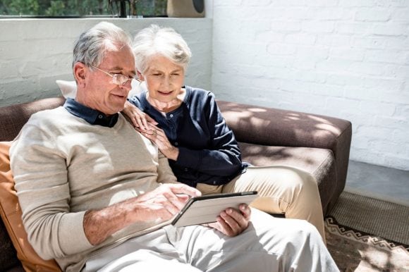 Senior couple sitting on the sofa reading a tablet computer and socializing.