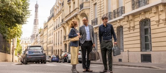 Tres personas hablando en una calle de Paris con la Torre Eiffel a la distancia