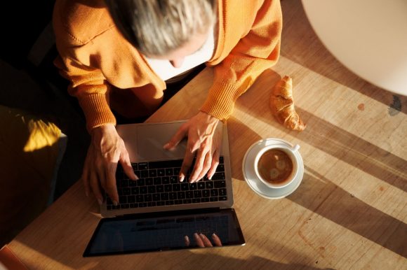Una mujer inversionista sentada en una mesa con su computador portátil y un café.