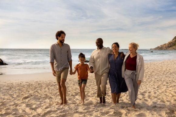 Família de três gerações caminhando juntos na praia de costas para o mar