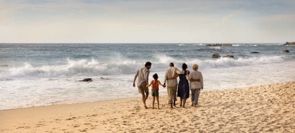 Família de três gerações na praia olhando para o mar