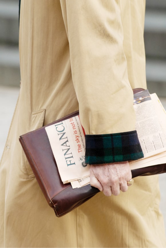 Uma pessoa andando pela rua segurando um jornal e uma pasta