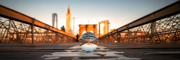 Glass sphere reflecting an upside-down row of colourful buildings on a sunlit street.