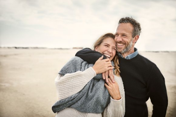Una pareja sonriente abrazándose en una playa brumosa