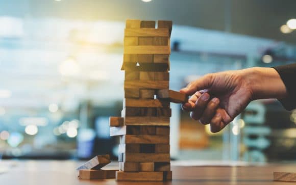 hand of businessman pulling out or placing wood block on the tower in modern office.