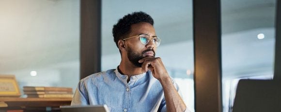 Man with glasses viewing computer screen and tablet