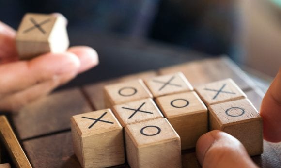 Hands placing wooden “X” and “O” blocks during a game of Tic-Tac-Toe