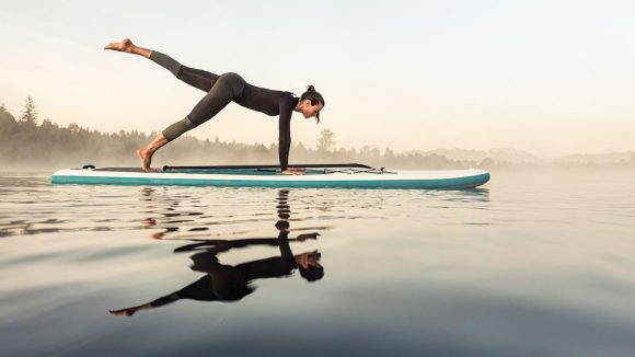 Women balancing on a paddle board in a lake.