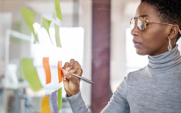 Person writing on sticky notes on a glass wall.