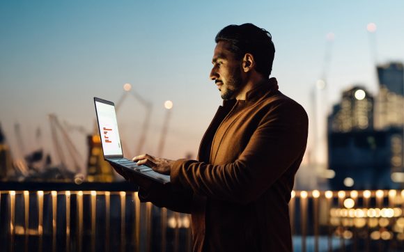 Man viewing chart on laptop with skyline in background