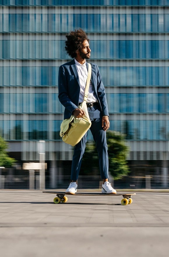 Young businessman riding on skateboard past a corporate building.