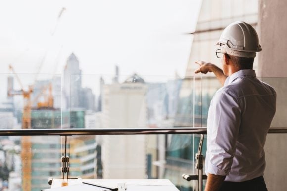 Portrait engineer man wearing safety helmet standing back and looking to the construction site with modern city background.