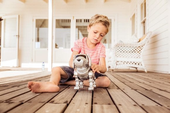 Young boy on front porch of house playing with robot dog