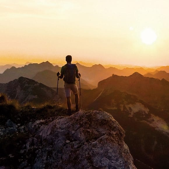 Hiker standing on mountain peak at sunset