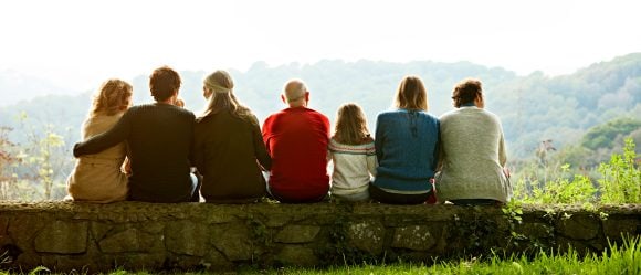 Rear view of multi-generation family relaxing in row on retaining wall against clear sky
