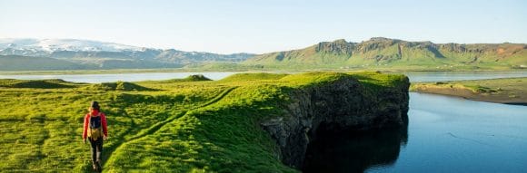 Man walking on a green small path on top of  a hill with panorama view on a big lake.