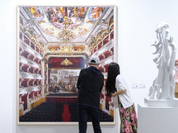 Two  visitors looking at a large-scale artwork depicting an ornate opera house interior.