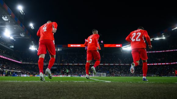 Soccer players in red uniforms take to the field for a night game under the lights of a large stadium