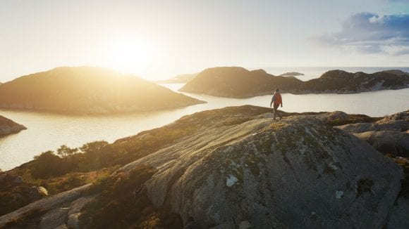 Man standing triumphantly at the mountain summit, bathed in beautiful sunshine.